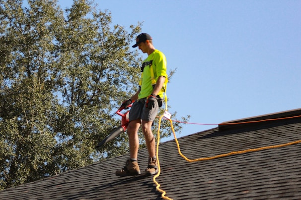 a man in a yellow shirt with a chainsaw on a roof