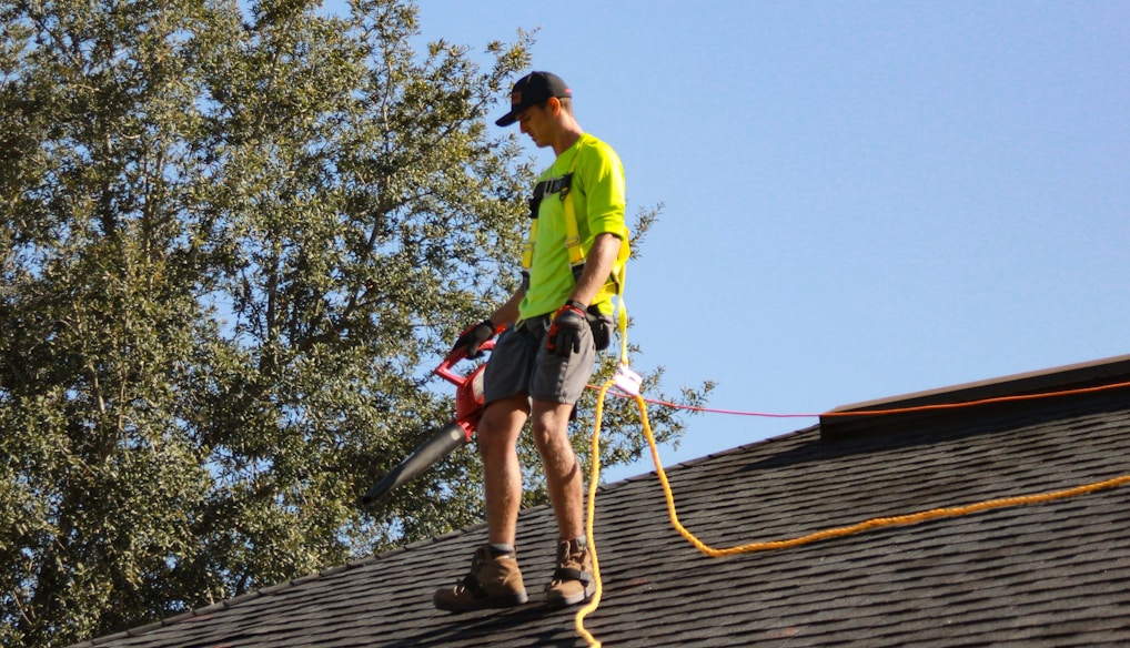 a man in a yellow shirt with a chainsaw on a roof