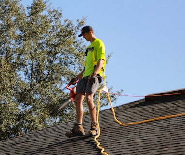 a man in a yellow shirt with a chainsaw on a roof