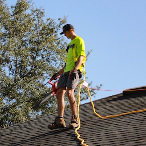 a man in a yellow shirt with a chainsaw on a roof