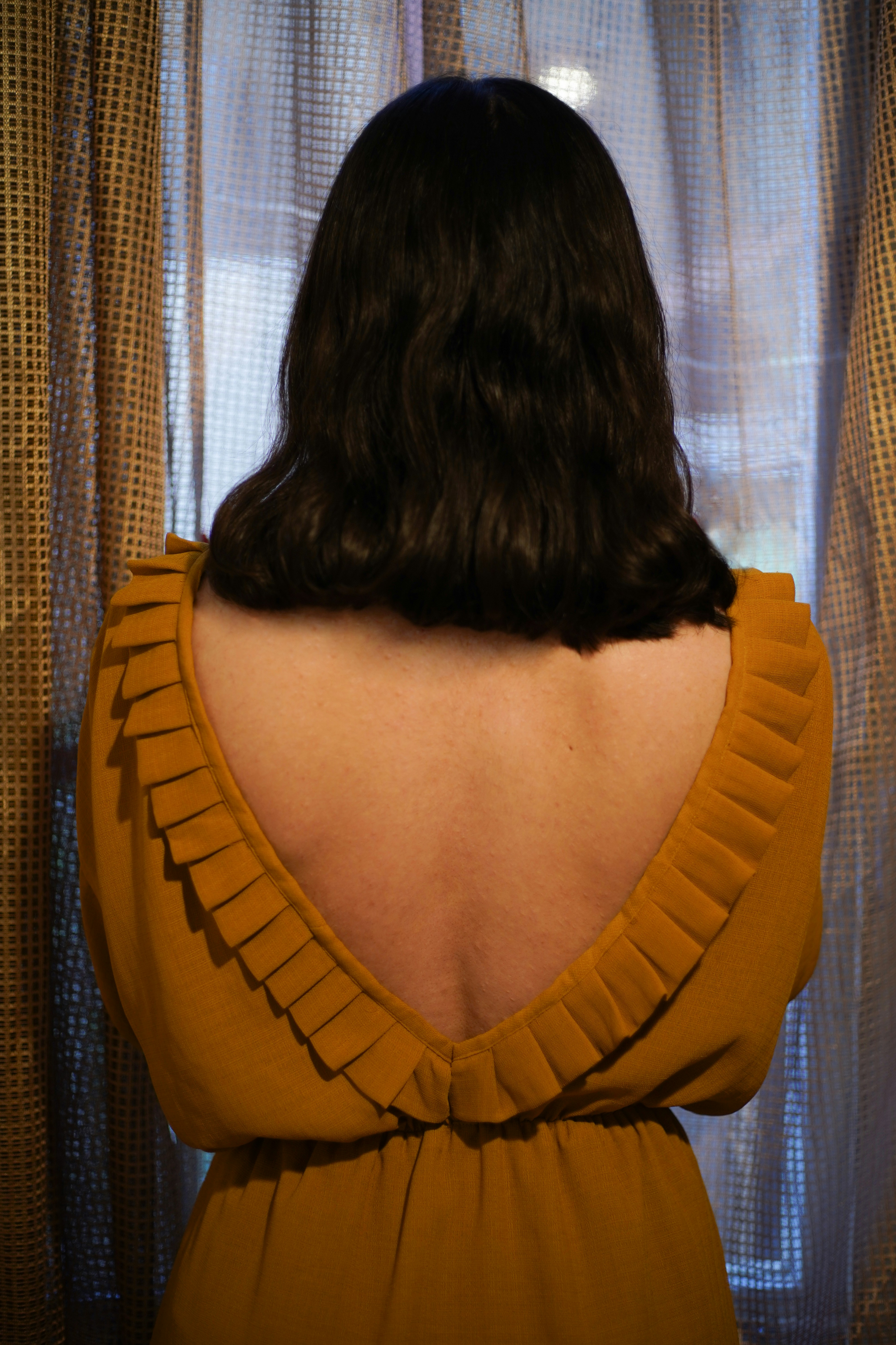 a woman standing in front of a window wearing a brown dress