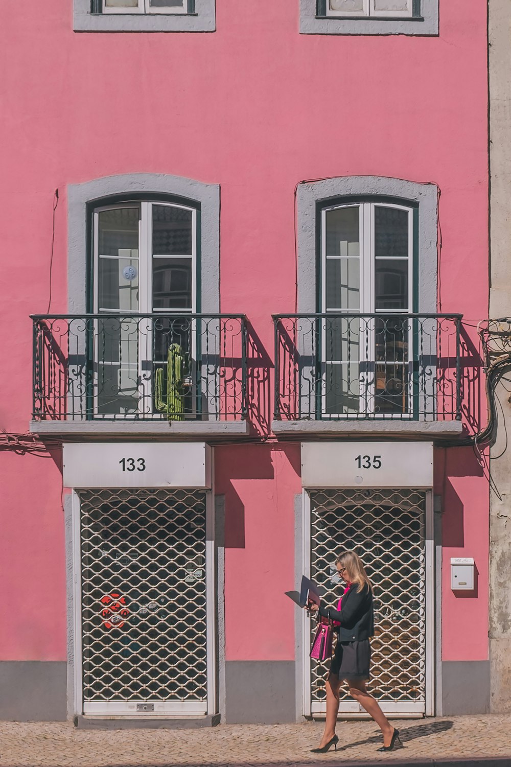 a woman walking down a street past a pink building