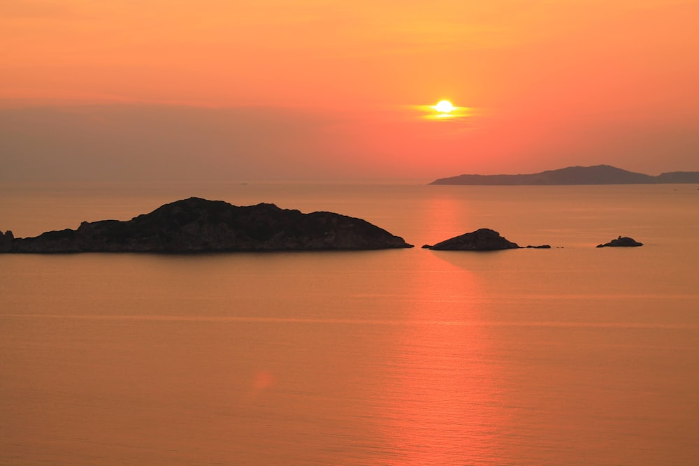a sunset over a body of water with a small island in the middle