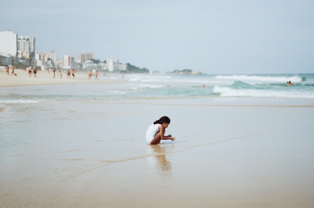 a woman kneeling down on a beach next to the ocean