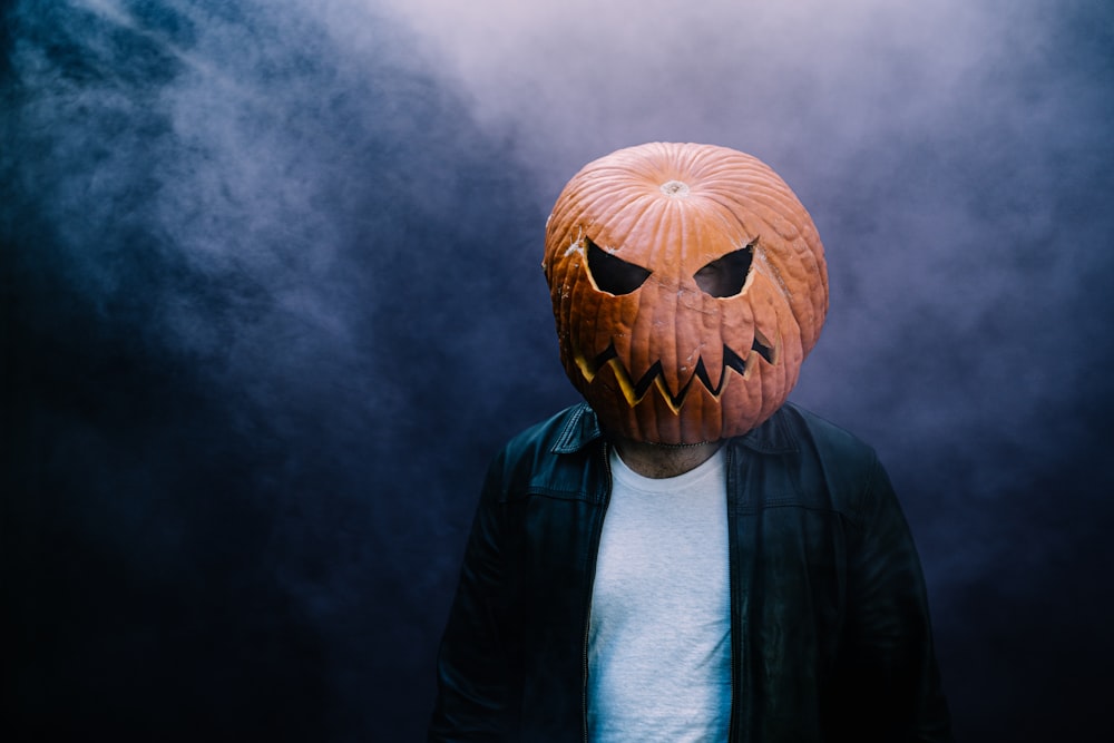 a person wearing a pumpkin mask on a dark background