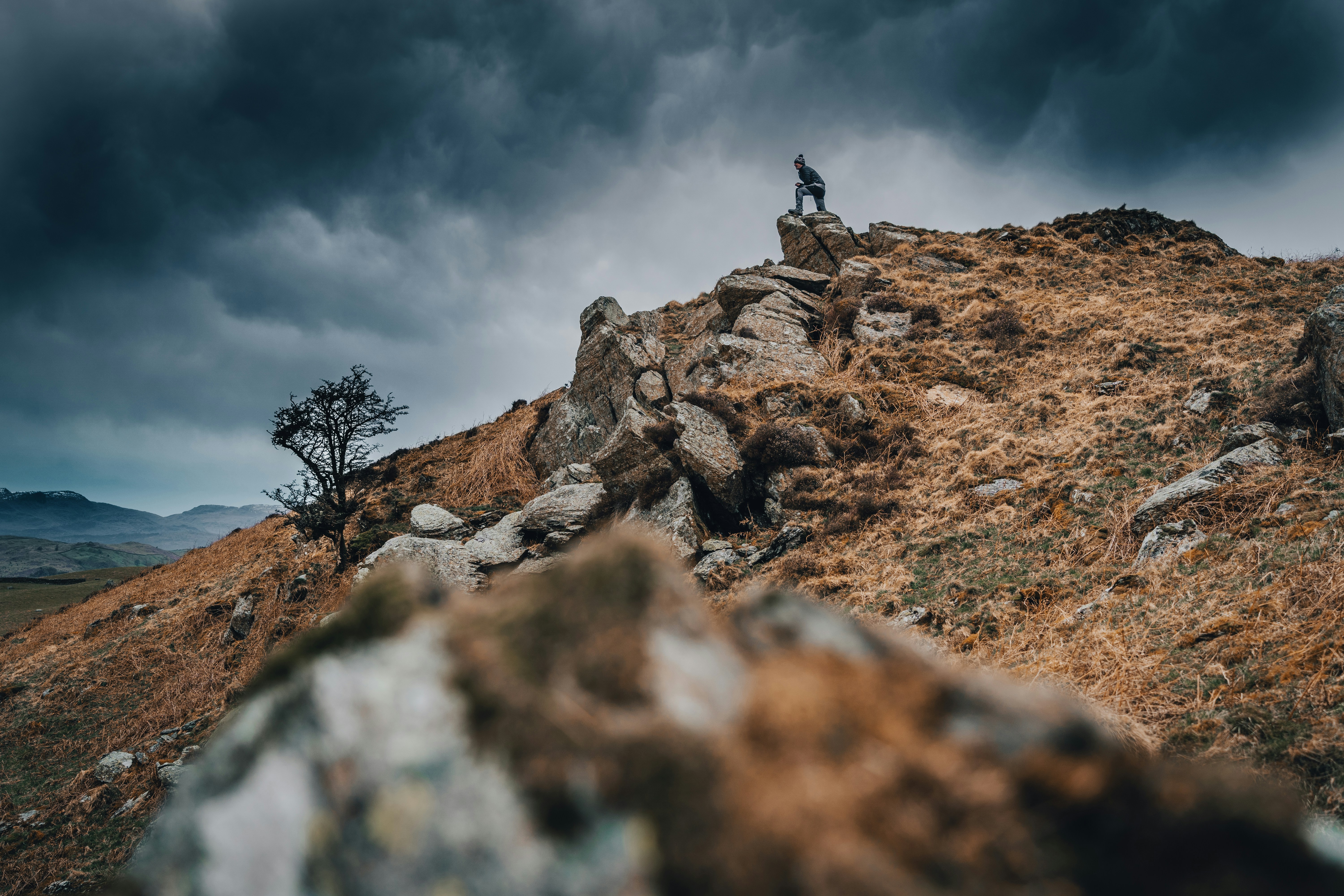 a man standing on top of a rocky hill under a cloudy sky