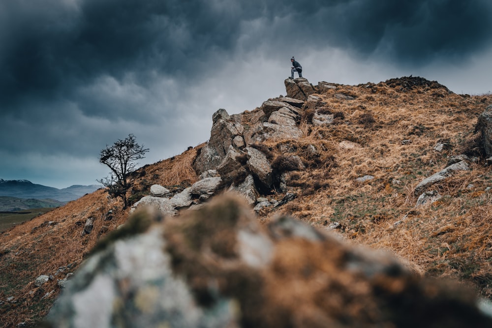 a man standing on top of a rocky hill under a cloudy sky