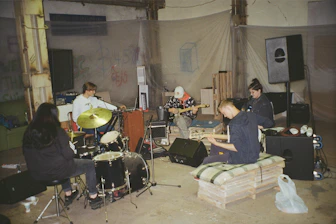 A group of young musicians jamming together in a cozy, well-equipped practice room.