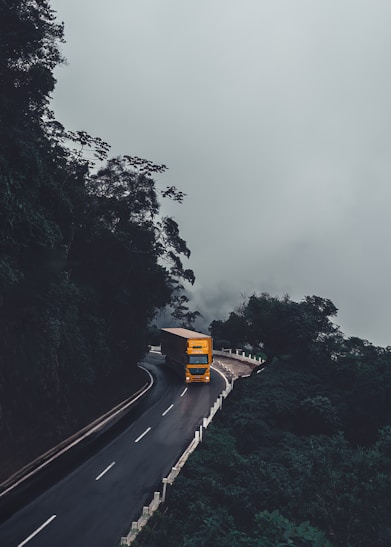a yellow bus driving down a road next to a forest
