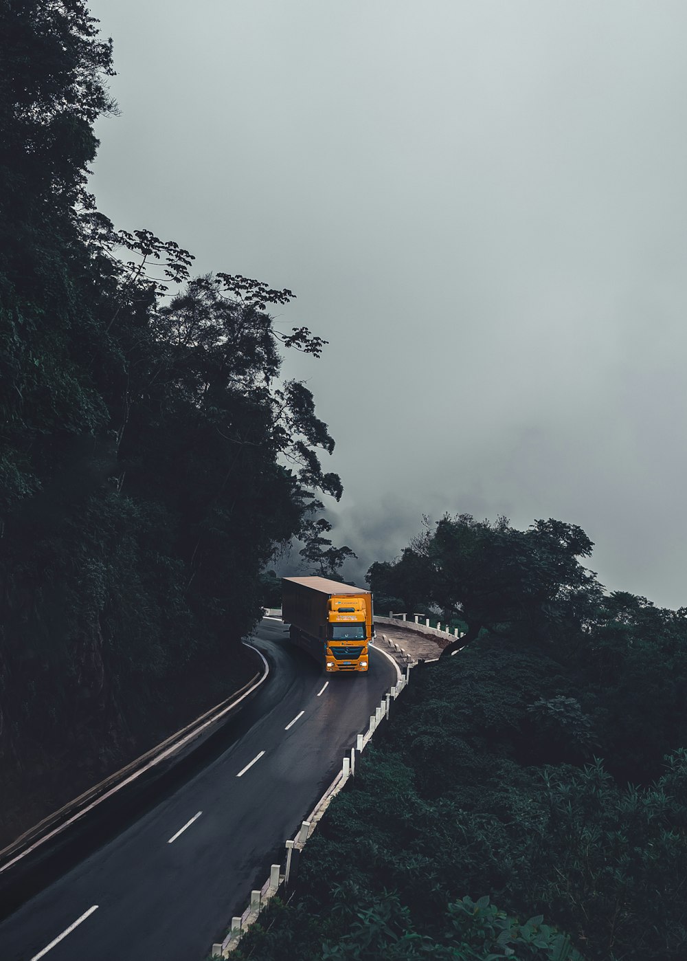 a yellow bus driving down a road next to a forest