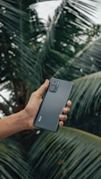 a hand holding a samsung s9 in front of a palm tree