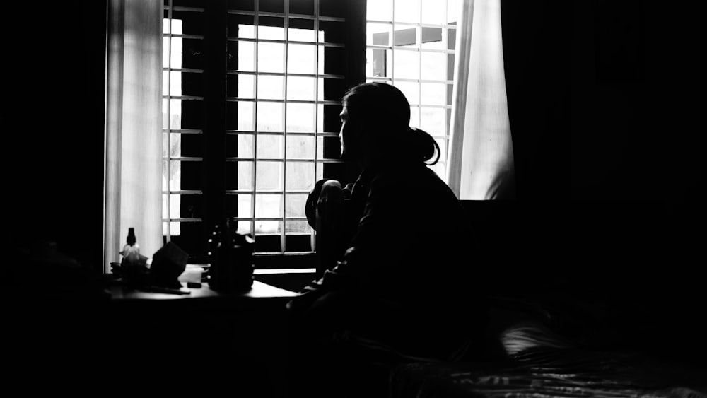 a black and white photo of a person sitting in front of a window