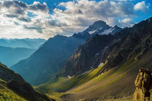 A deep valley in the Caucasus — Red and white house on green grass field near mountains under white clouds and blue sky