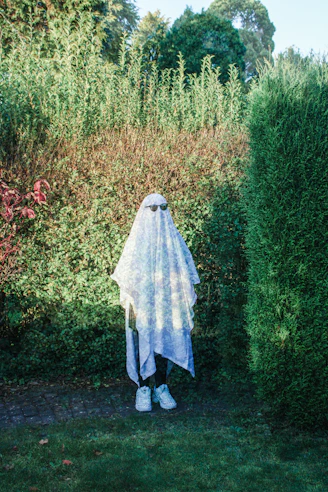 a woman in a white veil standing in front of a hedge