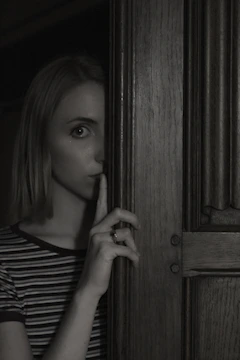 A close-up of a mysterious figure whispering in a dimly lit room filled with shadows.