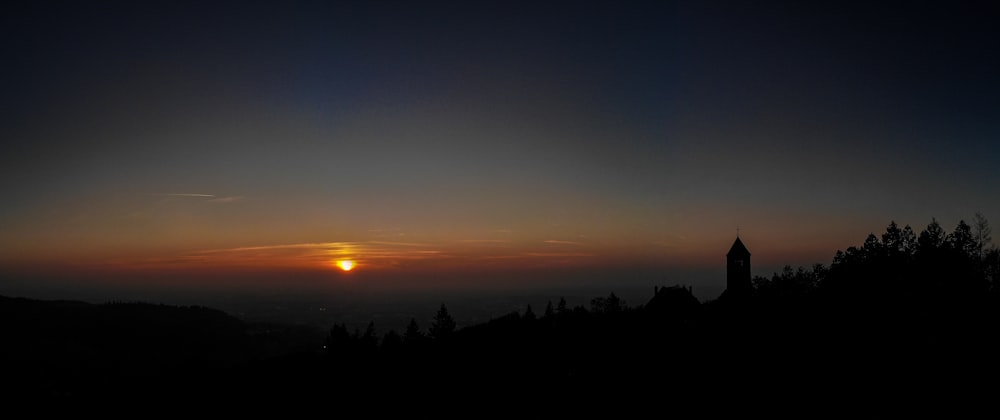 the sun is setting over a hill with trees