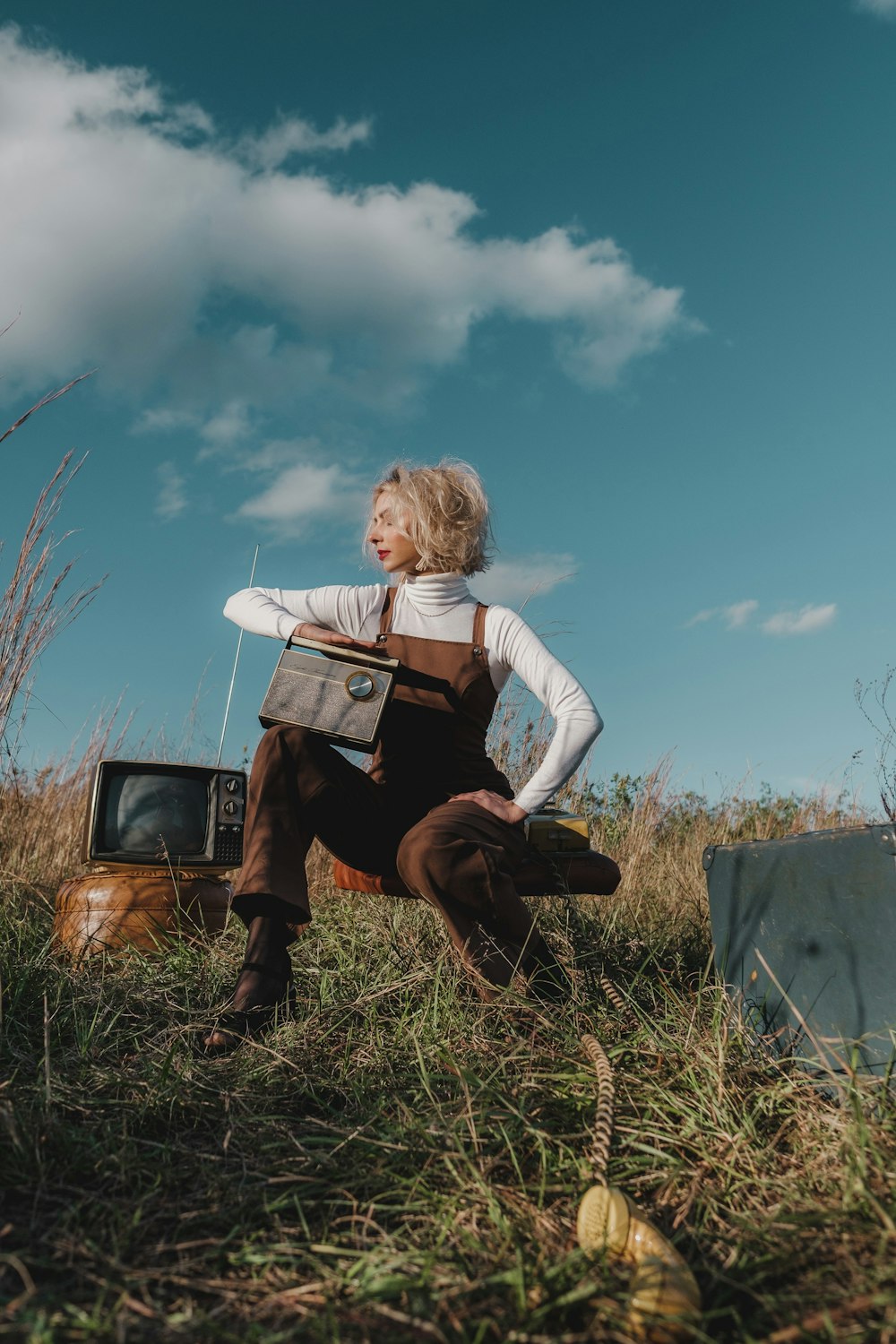 a woman sitting in a field next to an old tv