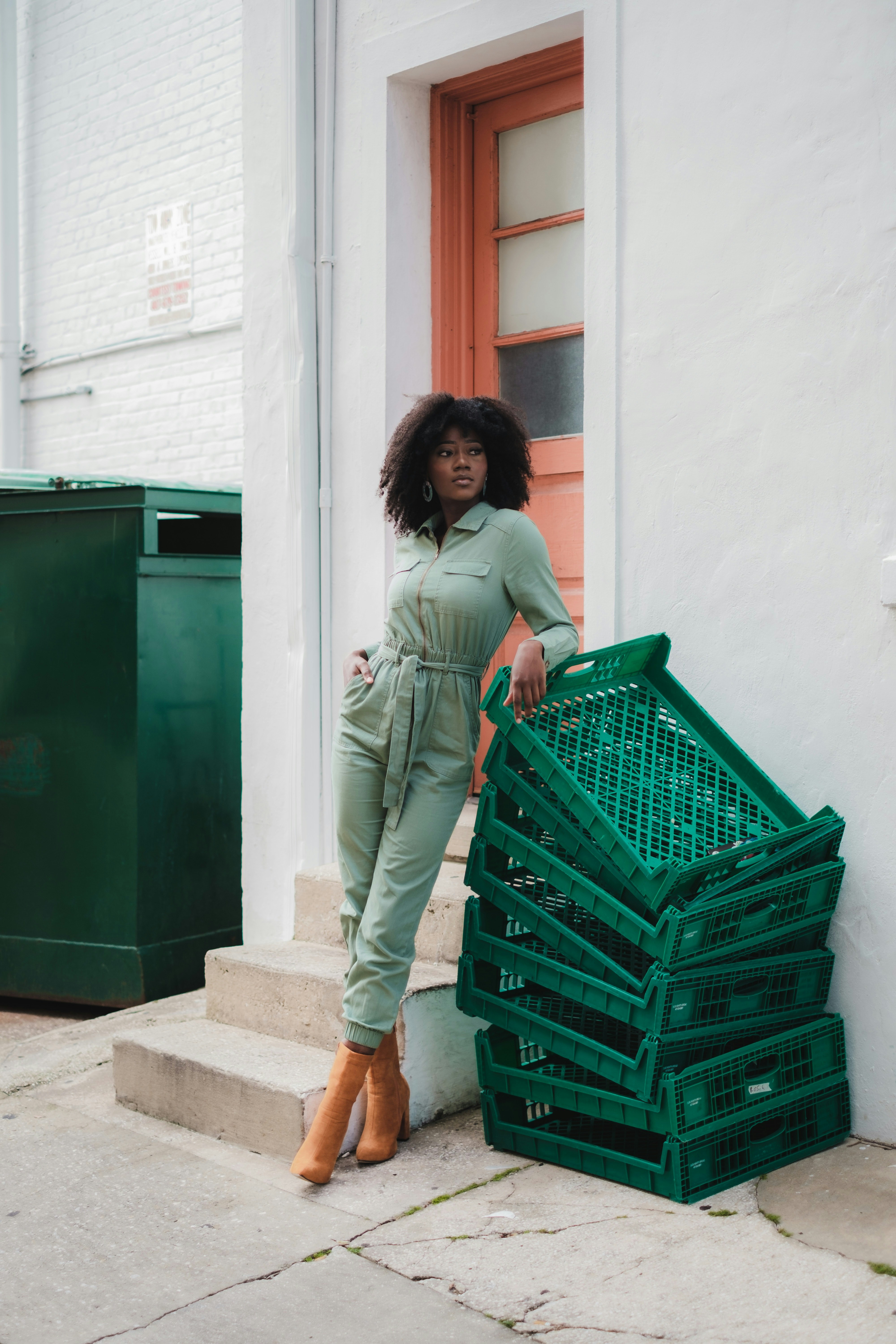 a woman in a green jumpsuit leaning against a stack of green crates