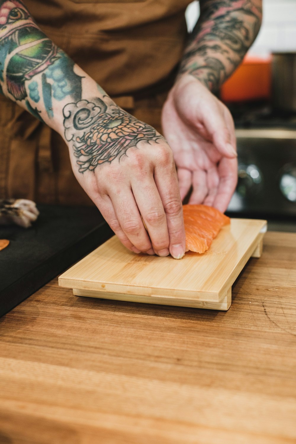 a man with a tattoo on his arm cutting up a salmon on a cutting board