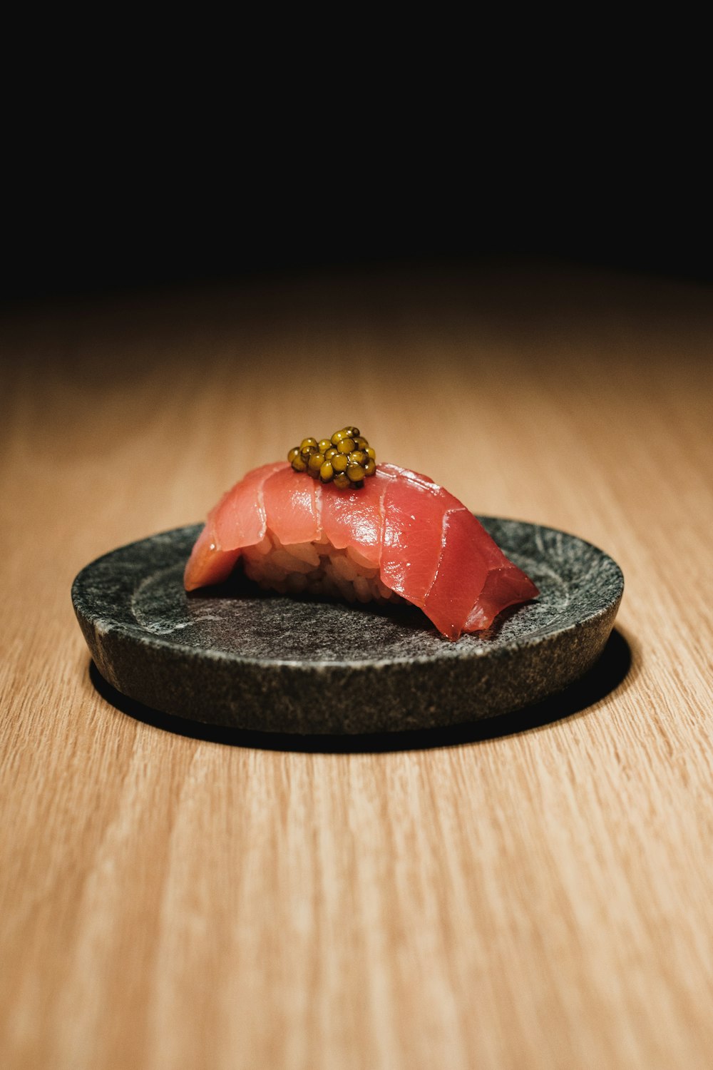 a piece of sushi on a black plate on a wooden table