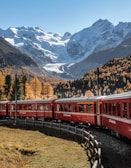 a red train traveling past a mountain covered in snow