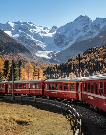 a red train traveling past a mountain covered in snow