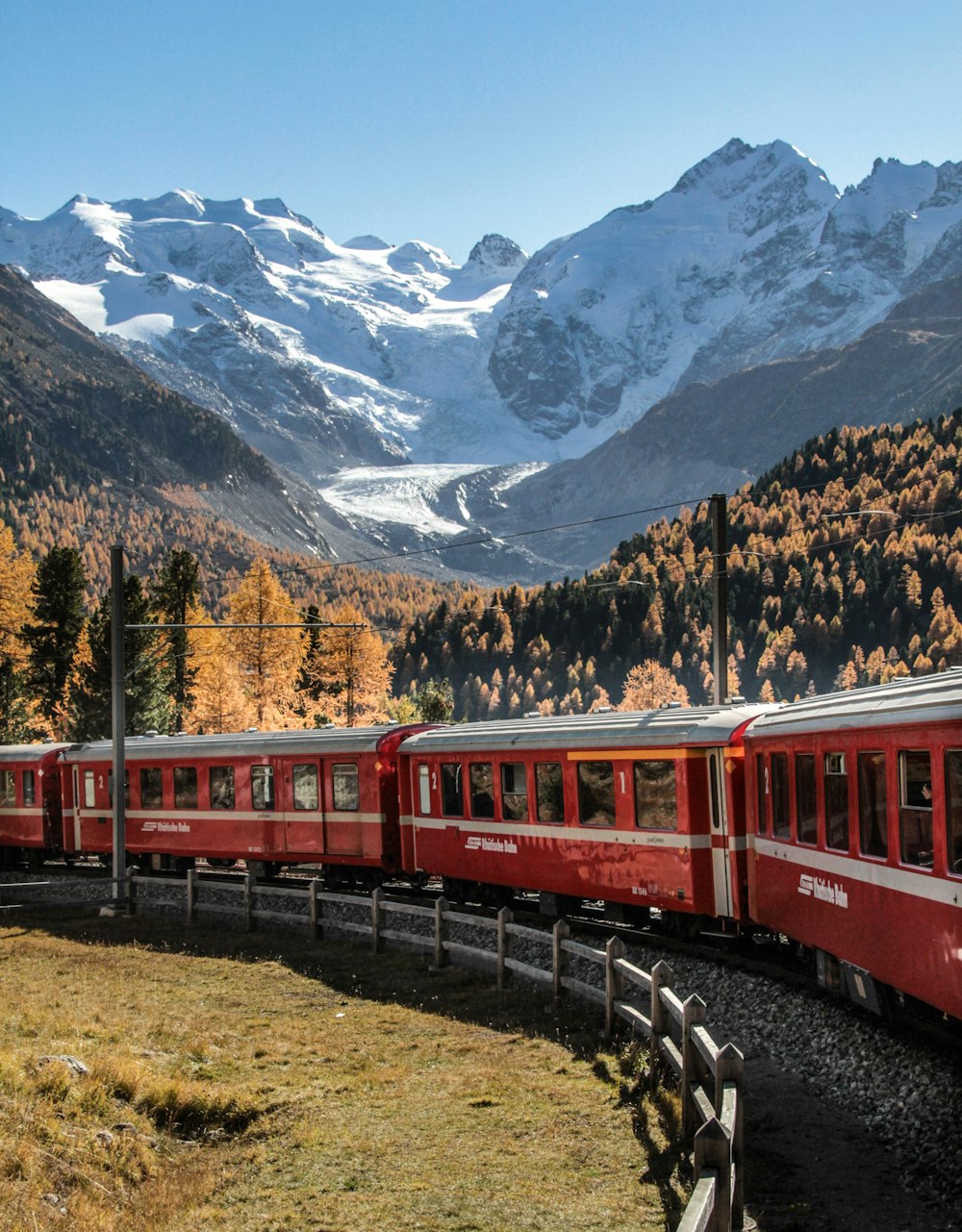 a red train traveling past a mountain covered in snow