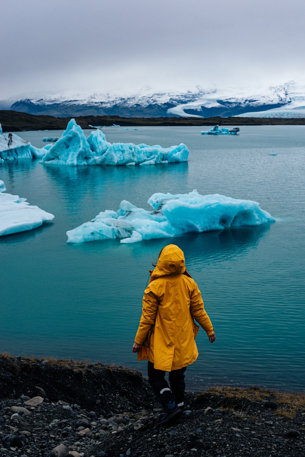 a person in a yellow jacket looking at icebergs