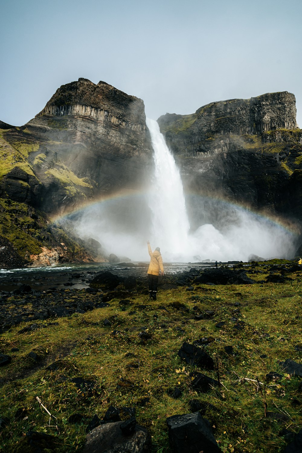 a person standing in front of a waterfall with a rainbow