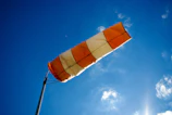A bright orange windsock fluttering against a clear blue sky on a sunny day.