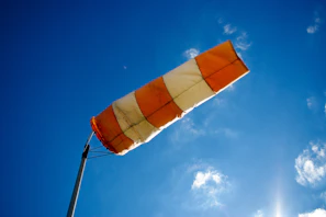 A bright orange windsock fluttering against a clear blue sky on a sunny day.