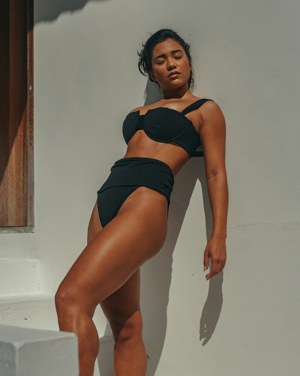 a woman in a bikini leaning against a wall