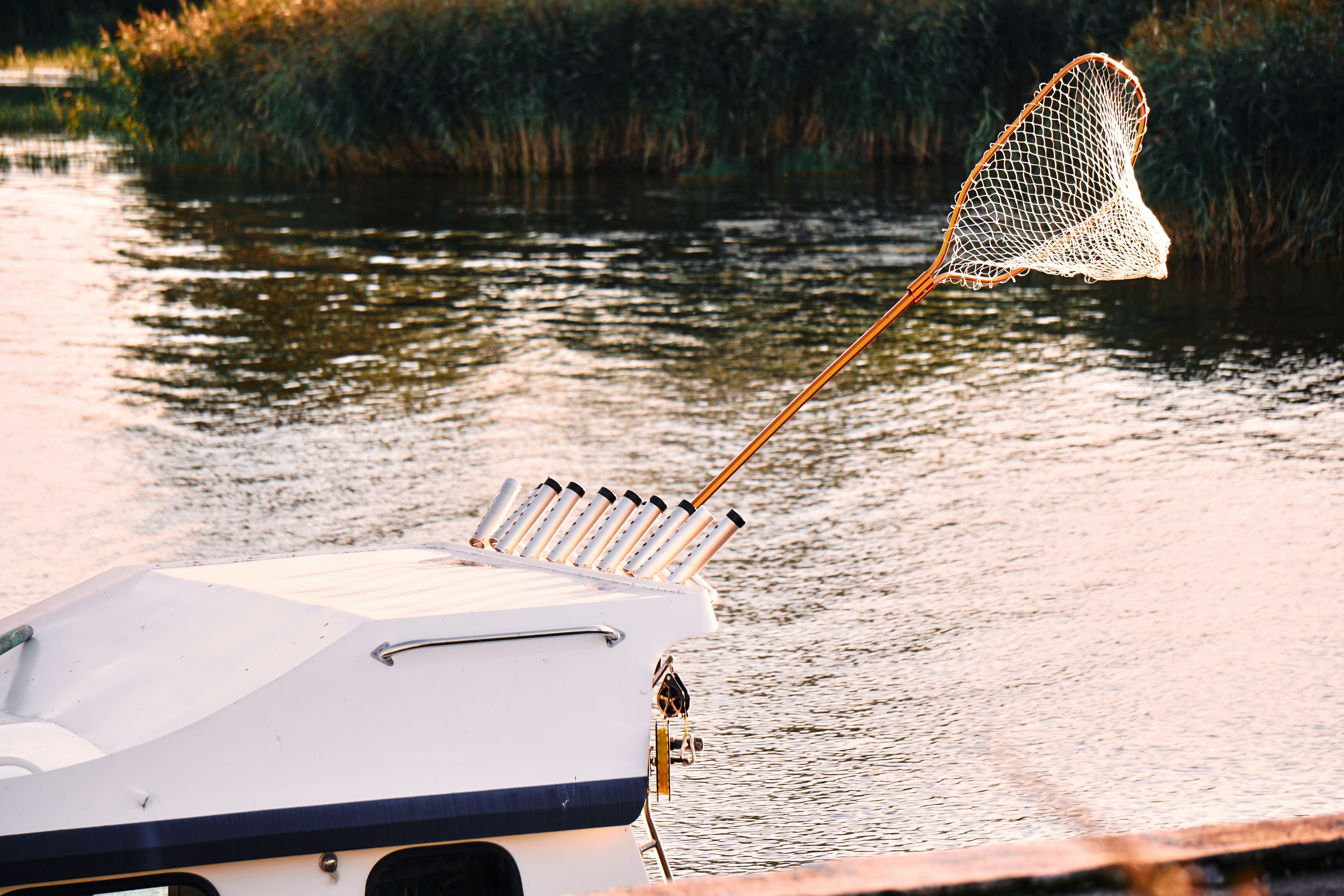 Landing net with a long wooden handle clipped upright at the stern of a small white boat on a calm marsh channel