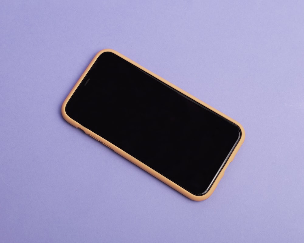 a black and gold cell phone laying on a purple surface