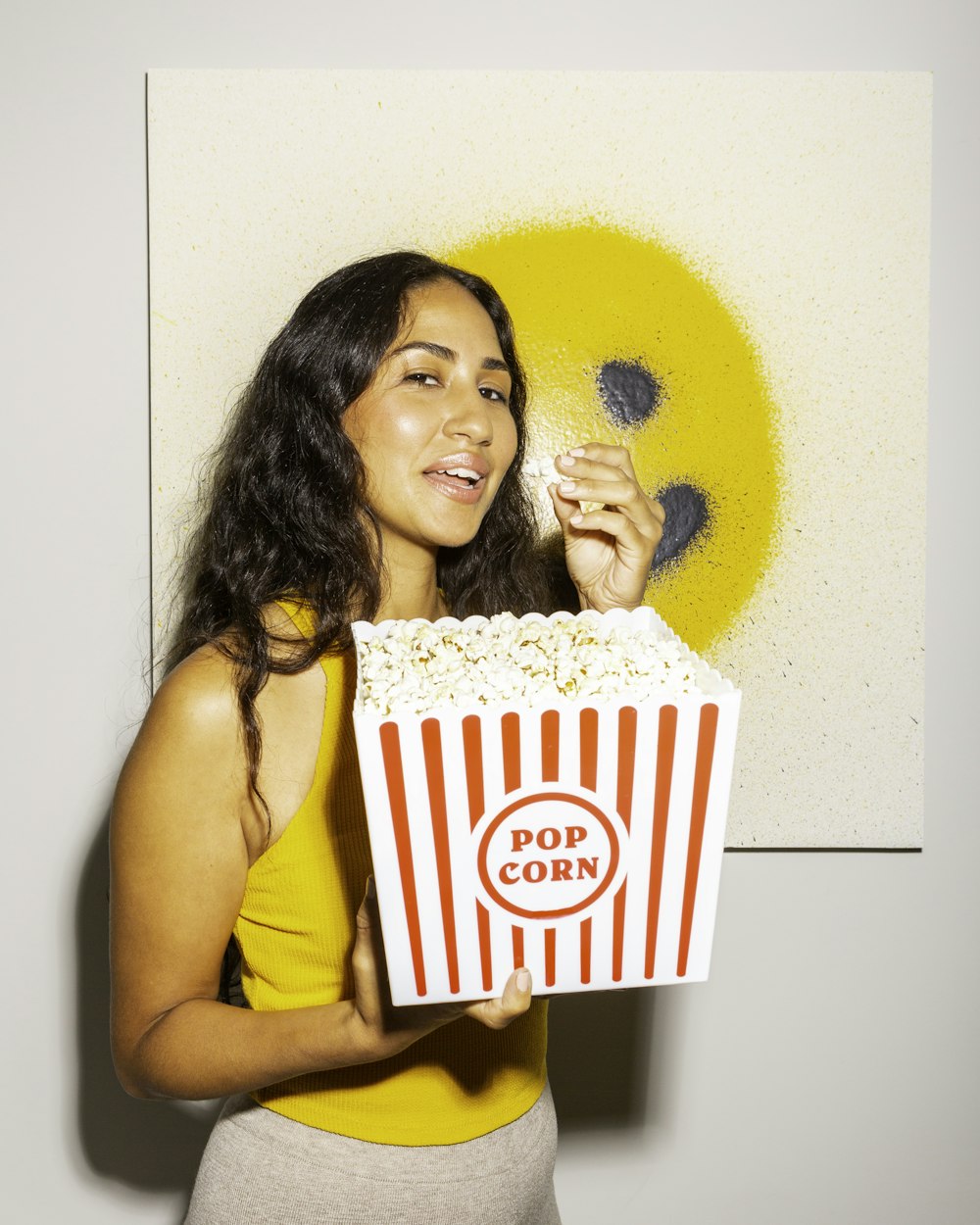 a woman holding a box of popcorn in front of a painting