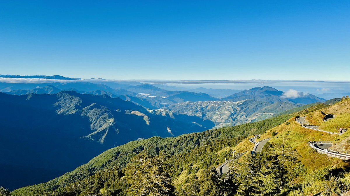 南投仁愛鄉合歡山一帶的高山公路蜿蜒在草坡上，遠方是層層山脈與雲海