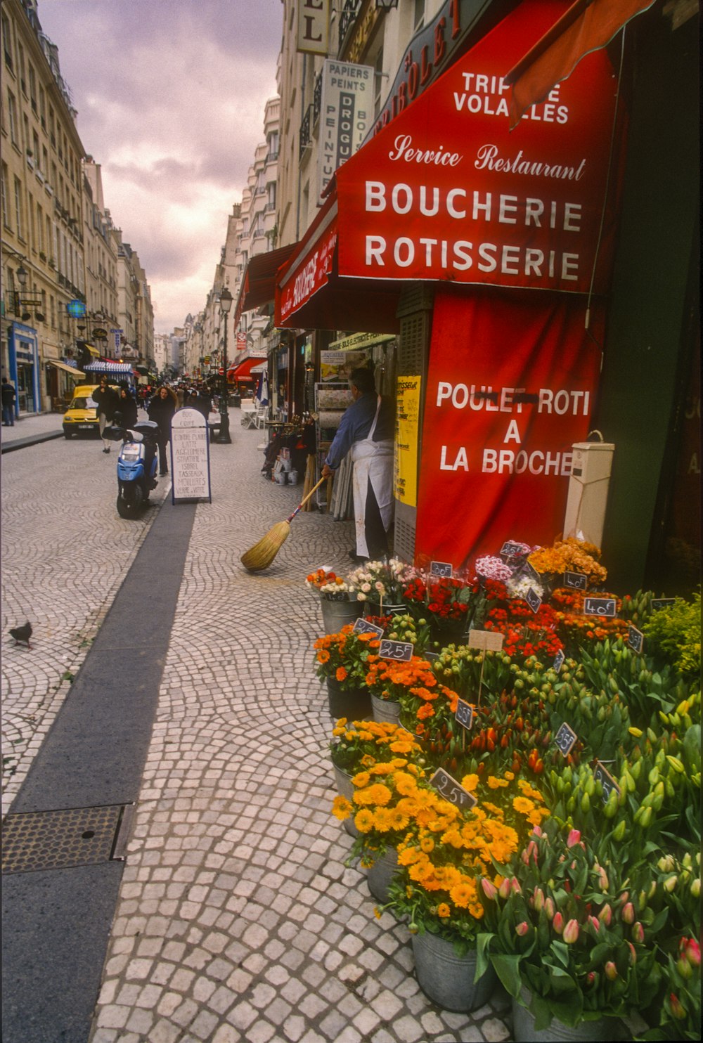 a cobblestone street lined with shops and flowers