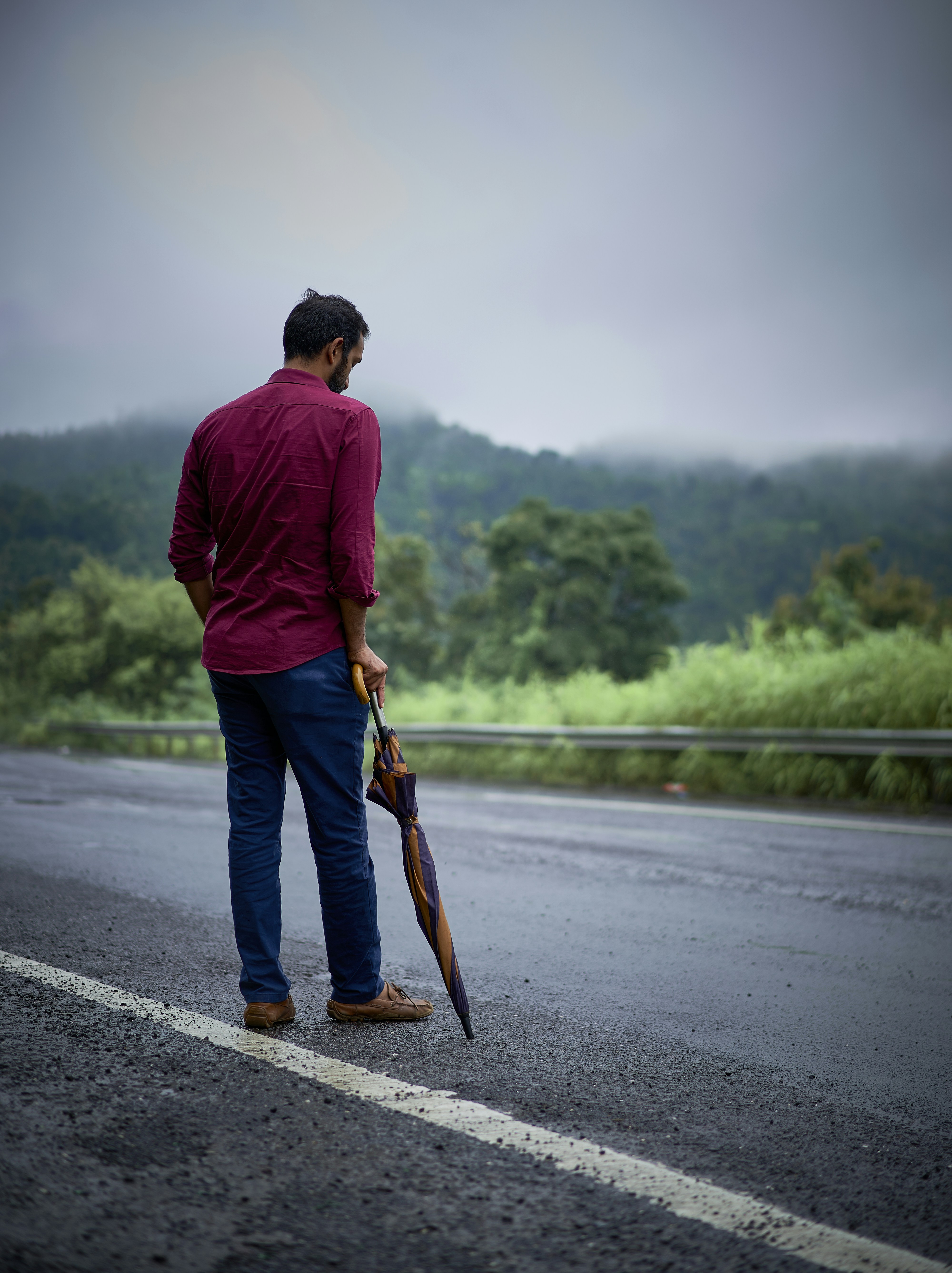 a man standing on the side of a road holding an umbrella
