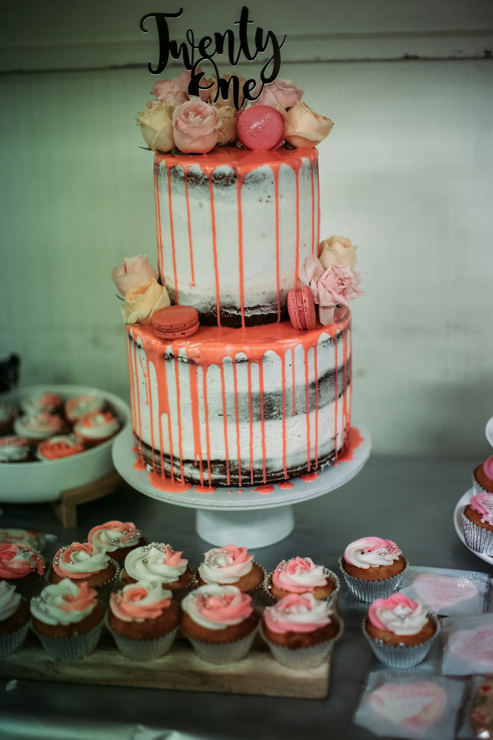 a three tiered cake sitting on top of a table next to cupcakes