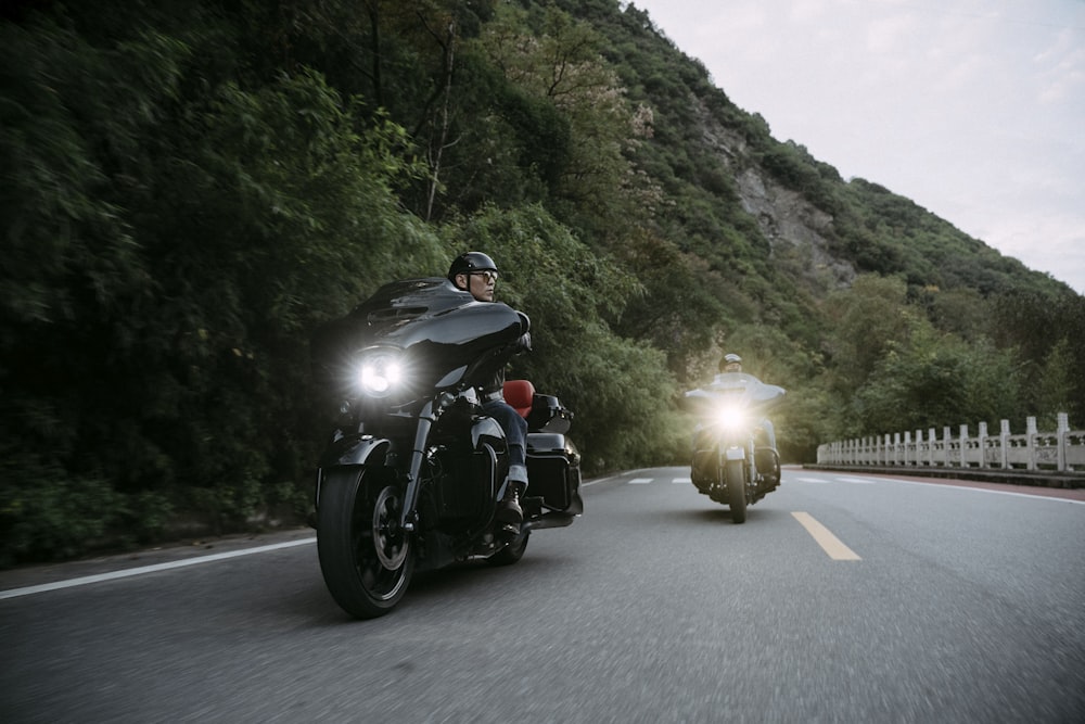 two people riding motorcycles on a road near a mountain