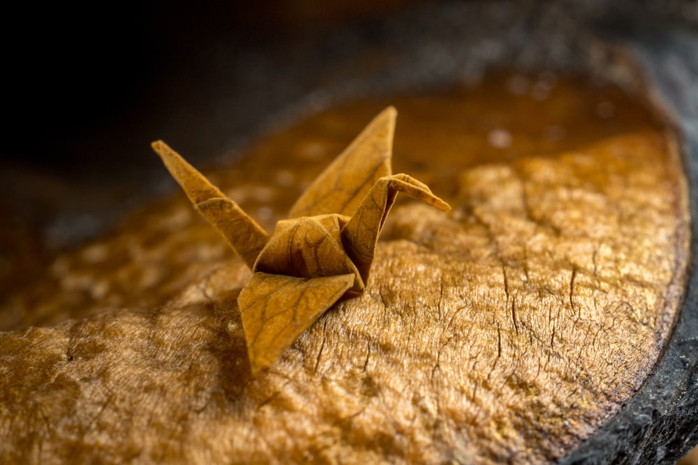 a yellow origami bird sitting on top of a piece of wood