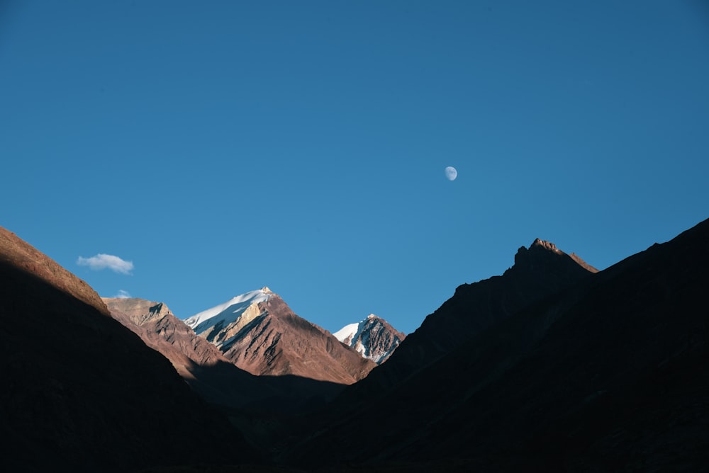 a mountain range with a half moon in the sky