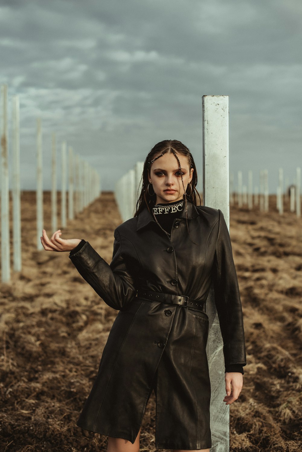 a woman in a black trench coat standing next to a pole