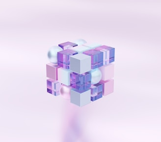 A geometric structure composed of translucent and opaque cubes and spheres arranged in a three-dimensional grid. The colors are primarily pastel shades of purple, pink, and blue, creating a soft and futuristic aesthetic against a pale background.