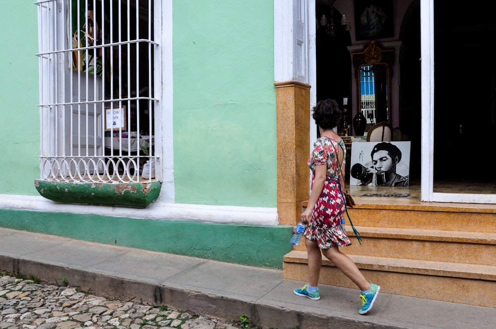 a woman walking down a sidewalk past a green building