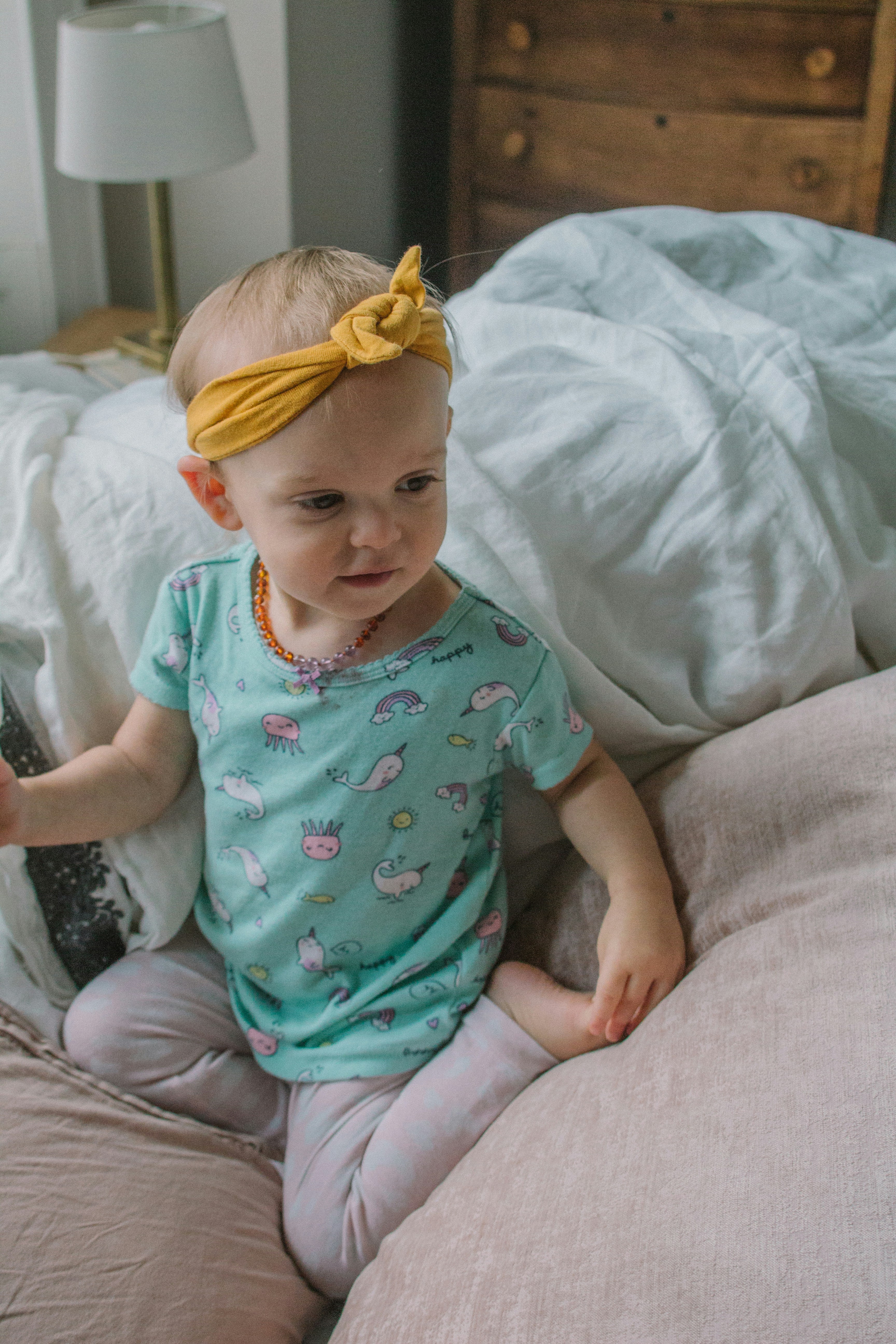 a little girl sitting on a bed with a yellow bow in her hair