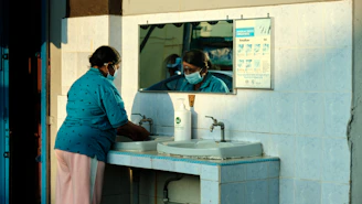 a woman wearing a face mask washes her hands in a sink