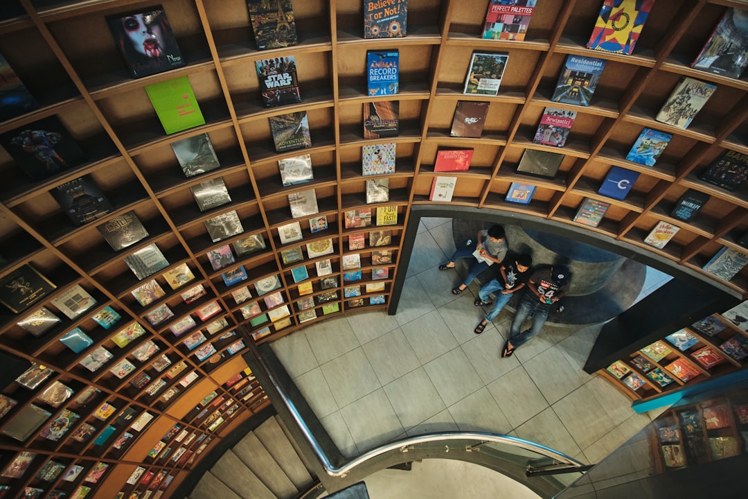 a group of people sitting on top of a book shelf, Father and sons resting next to a giant bookshelf in a bookstore.