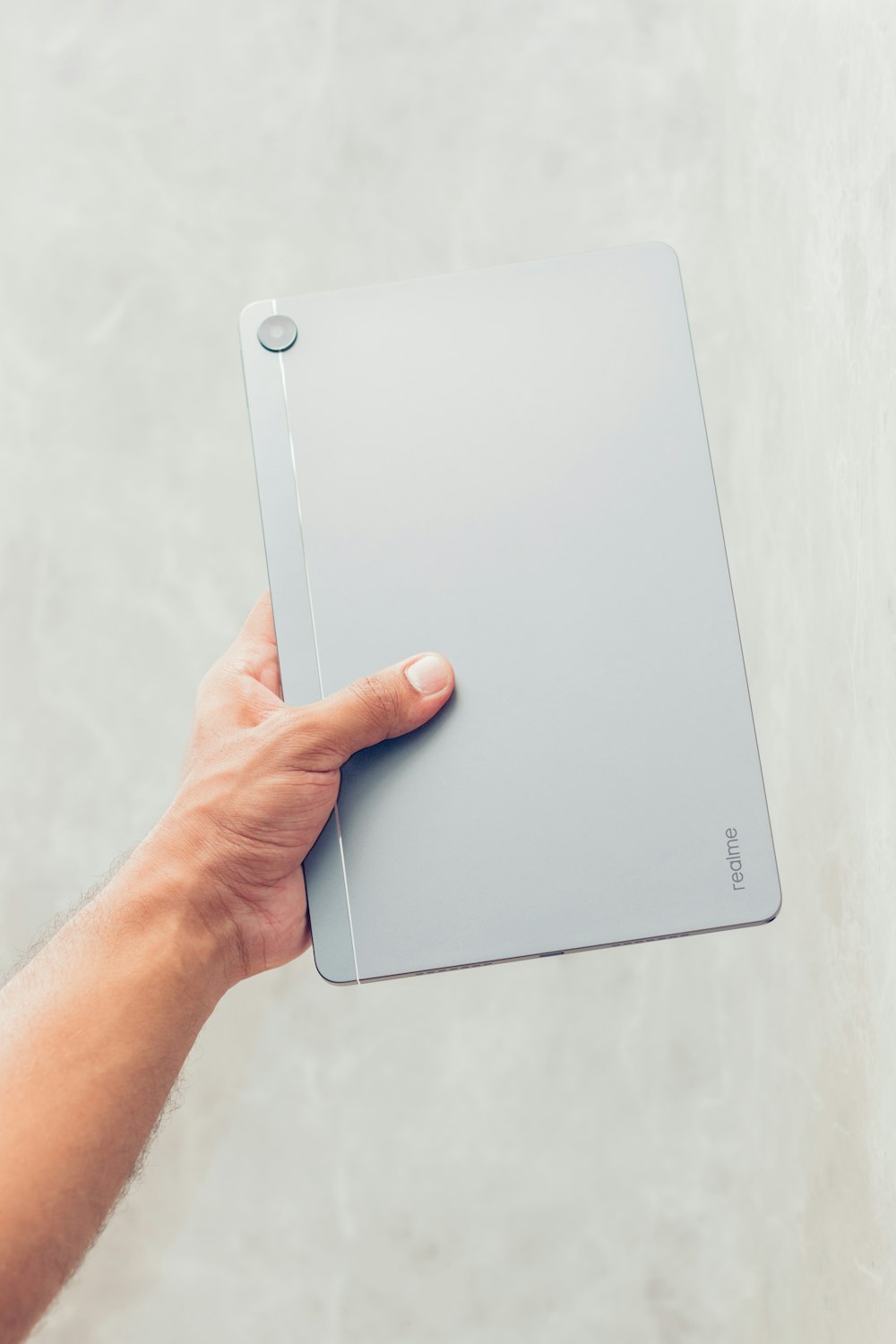 a hand holding a laptop computer in front of a white wall