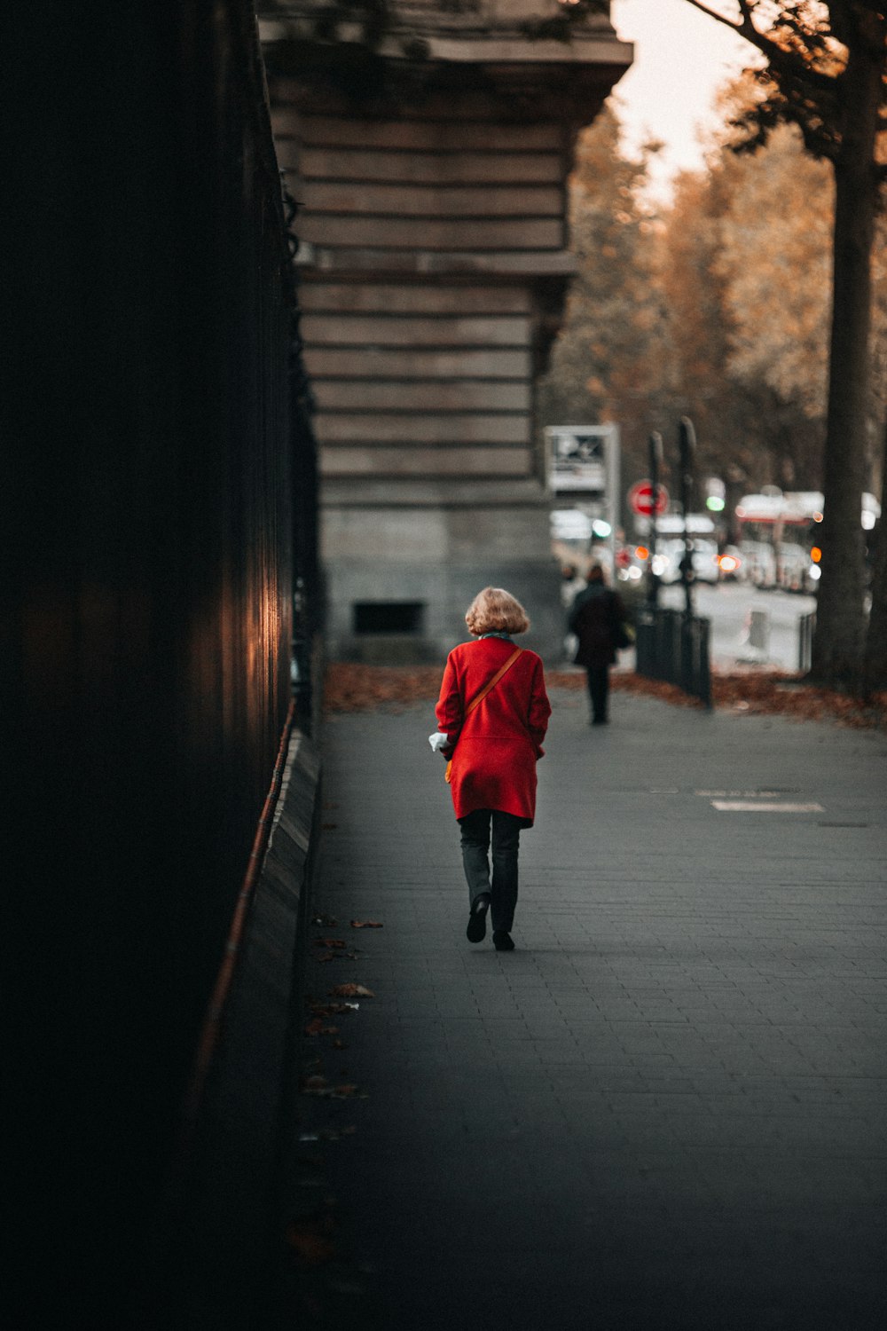 a little boy in a red coat walking down a sidewalk